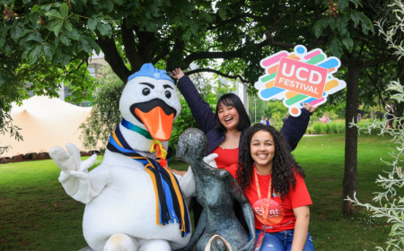 Two UCD Festival volunteers sitting at the Rendezvous statue with JJ the Swan.